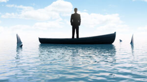 Business man in a suit standing in a boat being circled by sharks